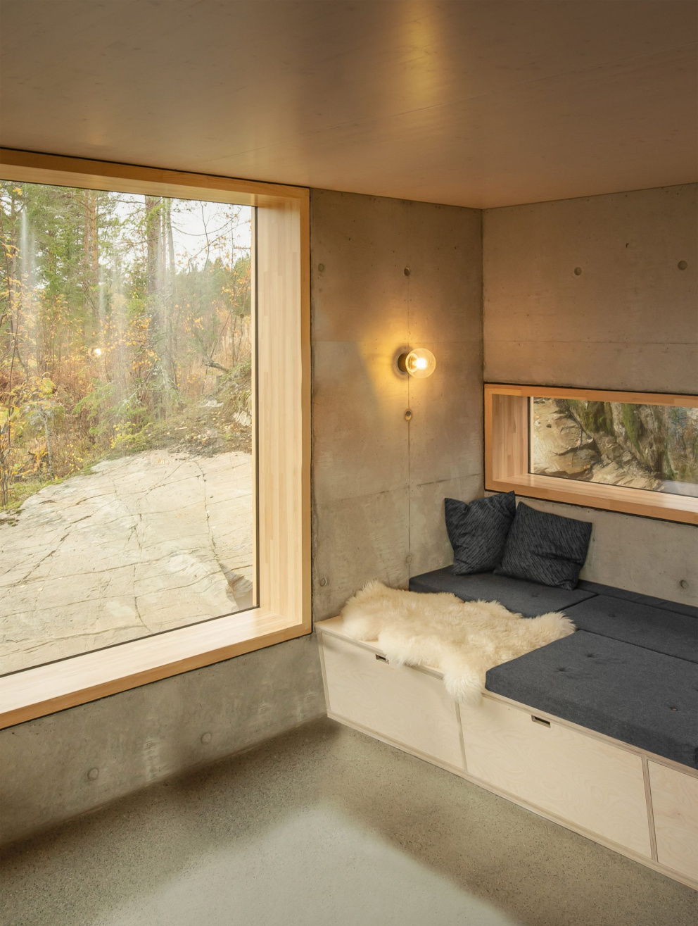 Surový beton krásně navazuje na skálu, na které je chata postavena. Útulnost a teplo dodávají interiéru přírodní materiály, jako dřevo a kožešiny.
