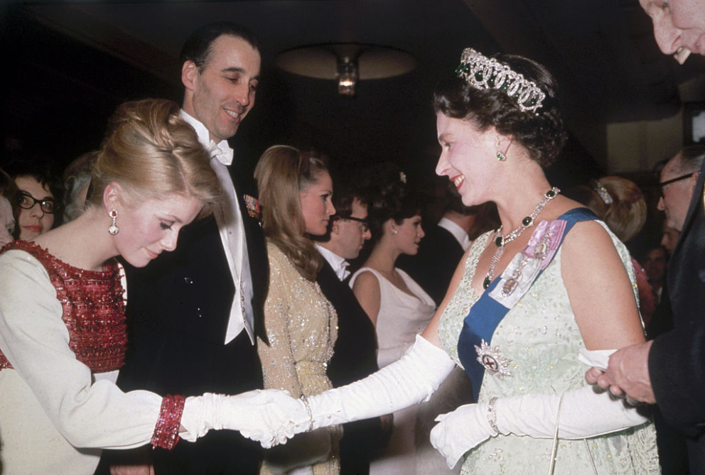 Francouzská herečka Catherine Deneuve se s Alžbětou II. setkala v roce 1966 v Londýně. Na sobě měla krémové šaty s červeným zdobením.
